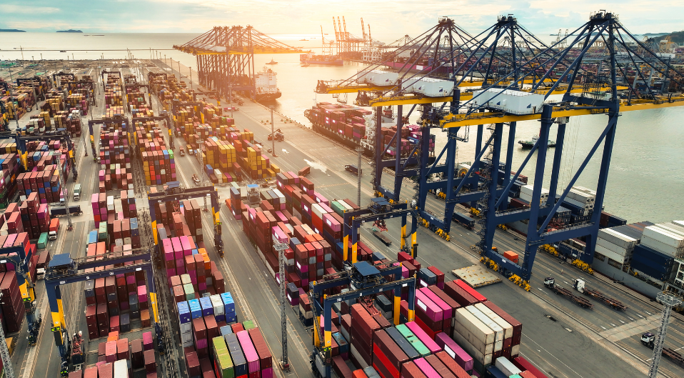 shipping containers stacked up on the concrete next to cranes at a shipyard
