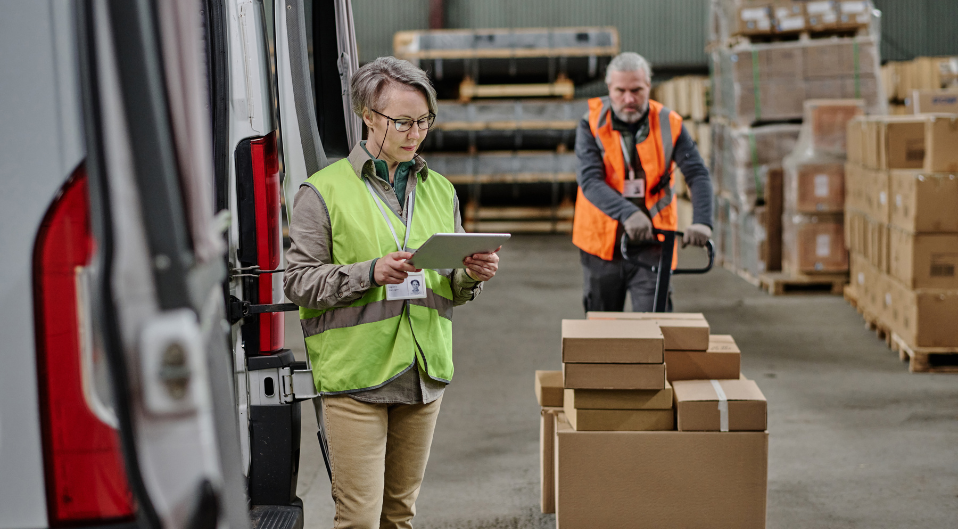 Distribution worker transporting parcels to a delivery van while a supervisor checks paperwork