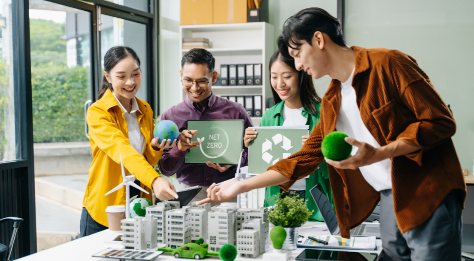 A group of business people standing around a conference table discussing net zero, recycling, sustainability, and emissions