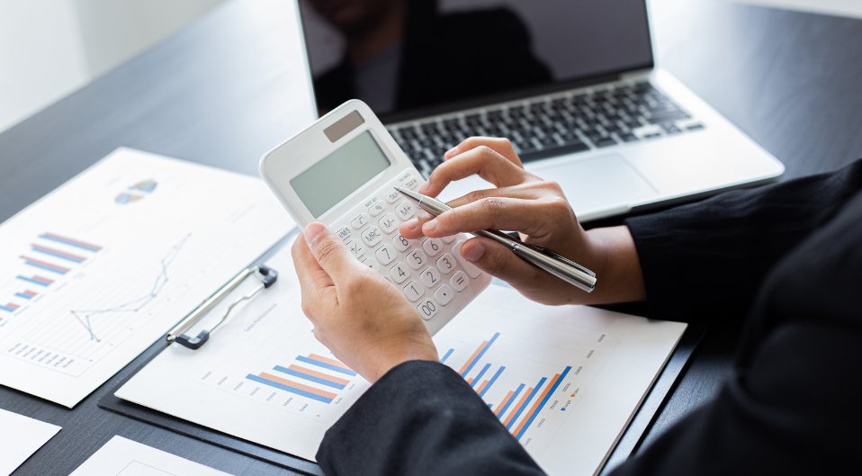 A business person surrounded by paperwork, calculating numbers on a calculator