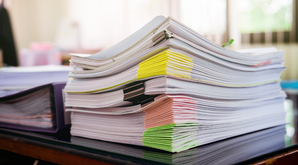A large stack of paperwork, banded together into bundles sorted by colour