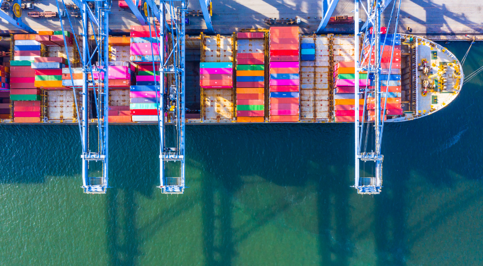 An overhead shot of cranes loading shipping containers onto a docked ship